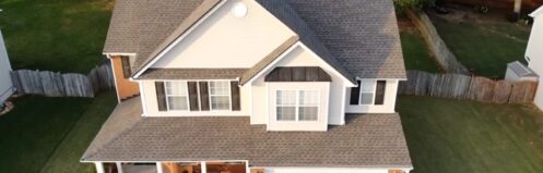 Two-story house with a gray roof, white siding, and well-manicured lawn and plants.