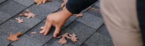 A person inspecting a roof covered with leaves, focusing on a specific area.