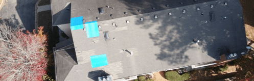 Aerial view of a residential building with blue tarps on the roof and autumn trees nearby.